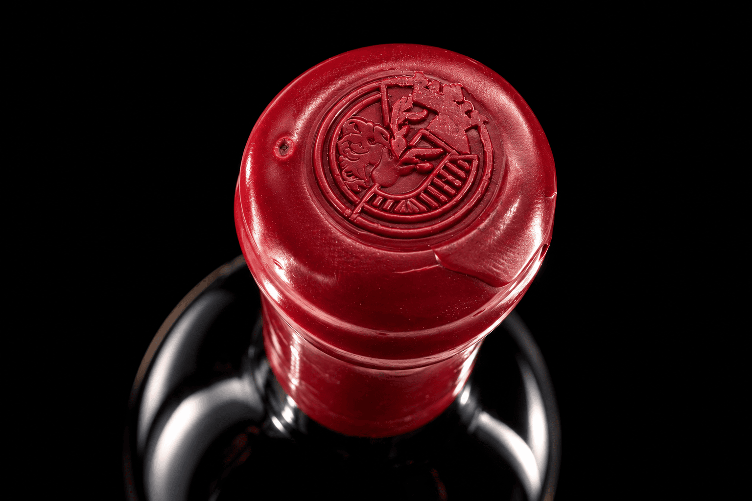 Close-up of a red wax-sealed wine bottle top with embossed logo.